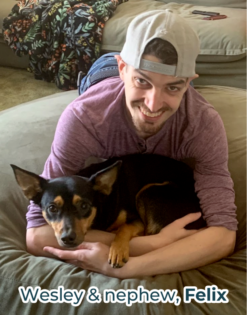 Photo of Wesley with his dog nephew Felix, a small black and brown dog, in his arms on a comfortable looking couch. 